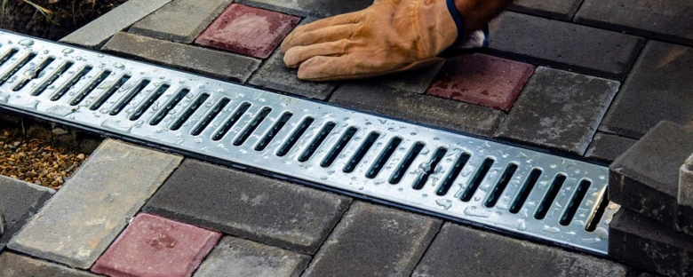 Instalace kovového žlabu do dlažby v zahradě s rukavicemi.