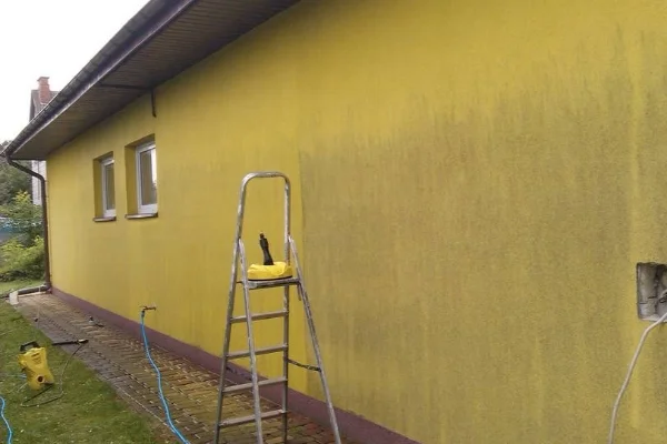 Žlutá fasáda domu s žebříkem pro čištění a renovaci.