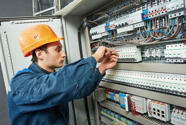Elektrikář pracuje na průmyslovém rozvaděči s kabely a jističi.