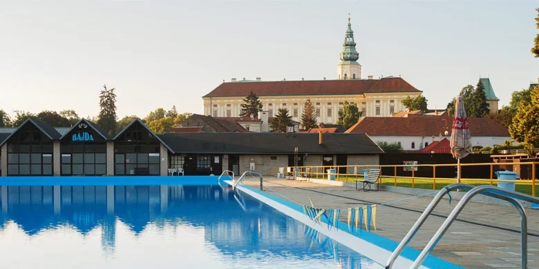 Venkovní bazén v Bajdě s historickým kostelem na pozadí.
