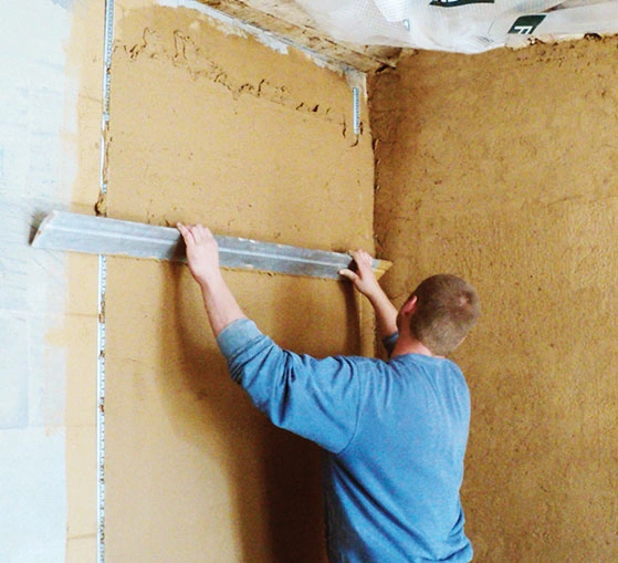 Muž nanáší jádrovou omítku na vnitřní zeď pomocí špachtle.