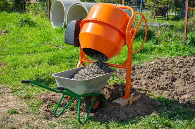 Oranžový betonová míchačka nalévá směs do vozíku na trávníku.