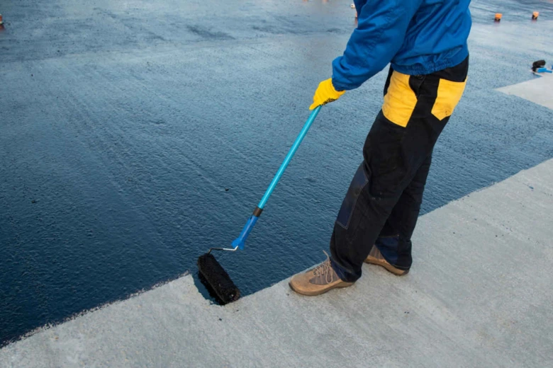 Pracovník nanáší tekutou hydroizolaci válečkem na betonovou plochu.