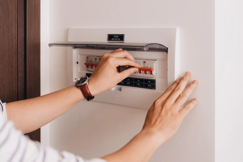 Ruka přepíná jistič v elektrickém rozvaděči.