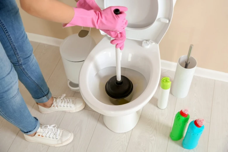 Člověk s růžovými rukavicemi uvolňuje ucpaný záchod pomocí hadice.