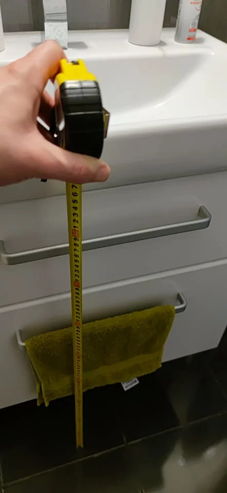 Ruční měření výšky umyvadla v koupelně páskou.