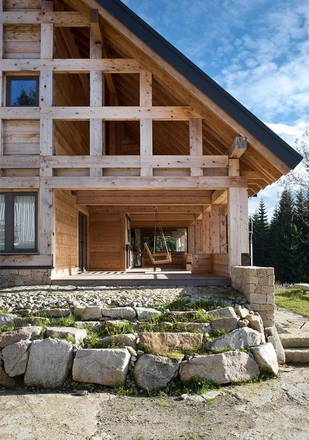 Moderní dřevěný dům s kamenným základem v přírodním prostředí.