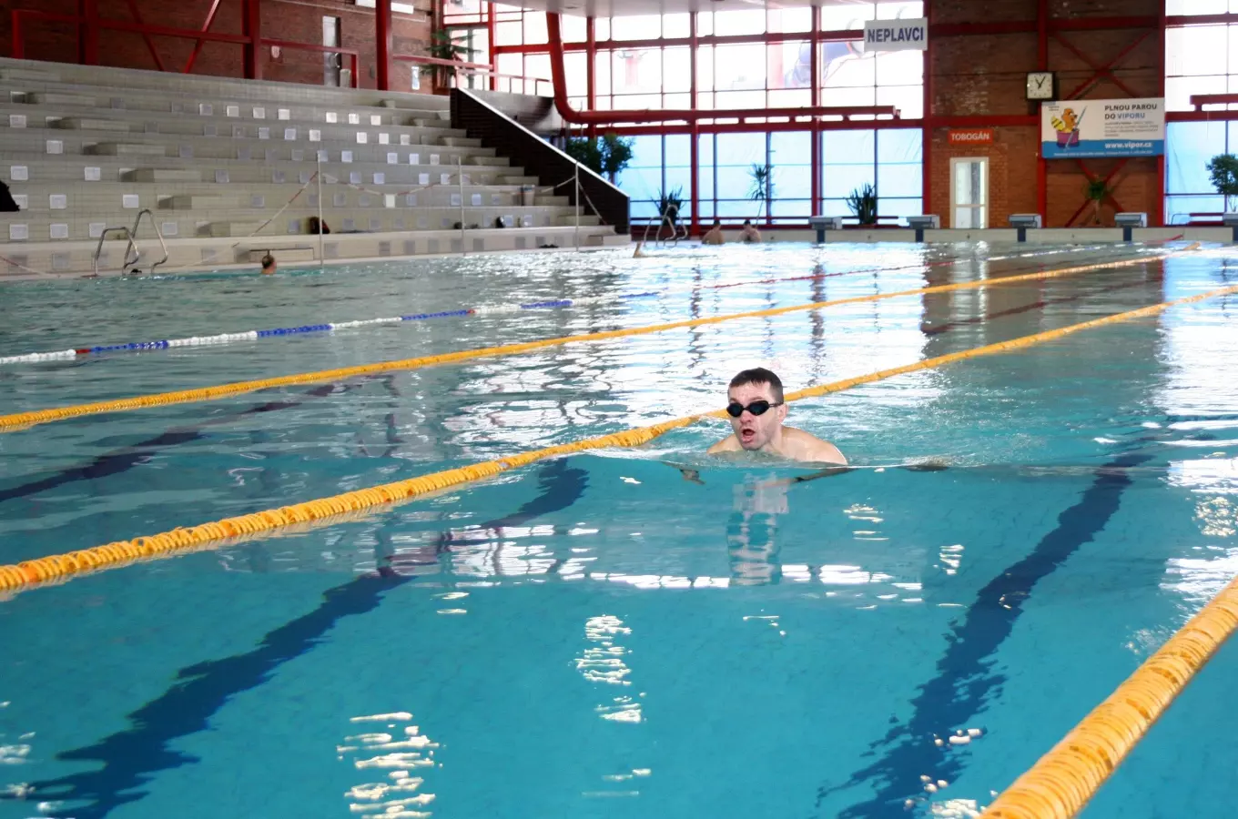Muž plave na zádech v krytém bazénu s dráhami.