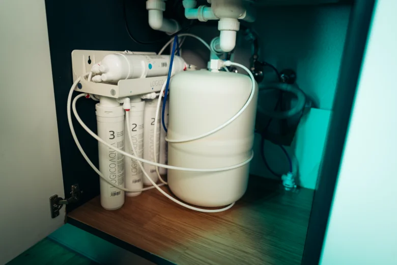 Bílý systém filtrace vody pod dřezem s viditelnými filtrami.