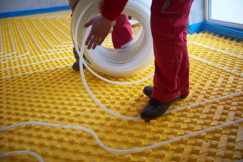 Instalace podlahového topení s trubkami na žluté desce.
