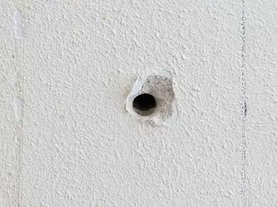 Malá díra v bílé zdi připravená na opravu tmelem.