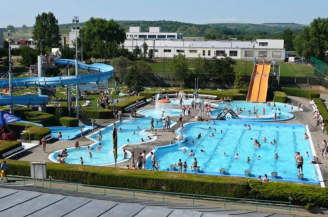 Venkovní bazén s vodními skluzavkami a lidmi v Hustopečích