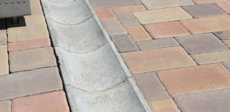 Konkrétní odvodňovací kanál mezi dlaždicemi kolem domu.