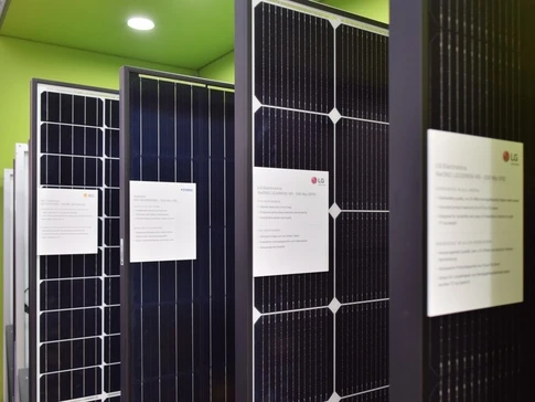 Řada fotovoltaických panelů s informačními štítky na zelené stěně.