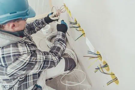 Elektrikář připojuje vodiče k zásuvkám ve zdi.