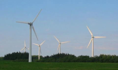 Větrné elektrárny na zeleném poli pod modrou oblohou.
