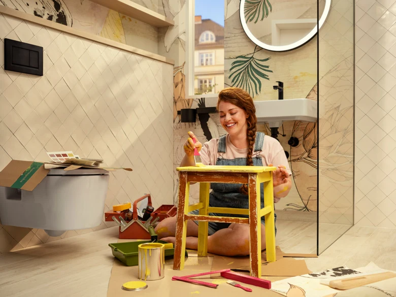 Žena maluje žlutou stoličku v moderní koupelně.