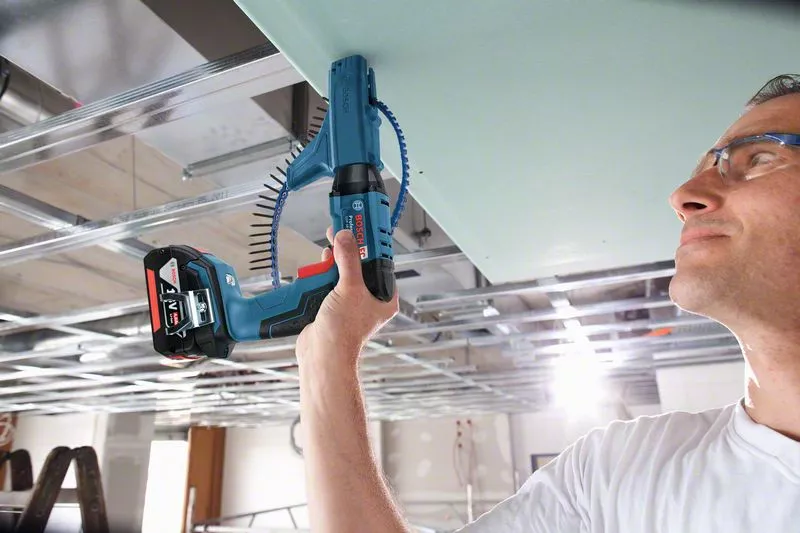 Muž montuje sádrokartonový strop pomocí elektrického nástroje.