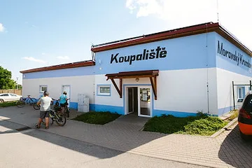 Vnější pohled na koupaliště v Moravském Krumlově s lidmi u vstupní brány.