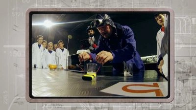 Muž v ochranném obleku ukazuje elektrický zkrat na stole.