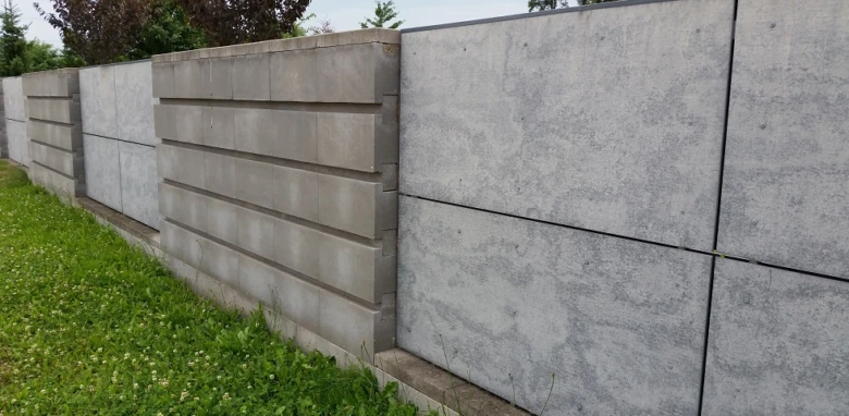 Řada šedých betonových plotů s horizontálními panely na trávníku.