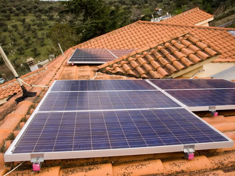 Fotografie modrých fotovoltaických panelů na střeše s červenými taškami.