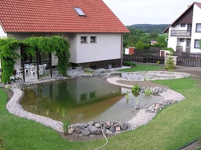 Zelené koupací jezírko v zahradě s kamenným obvodem.