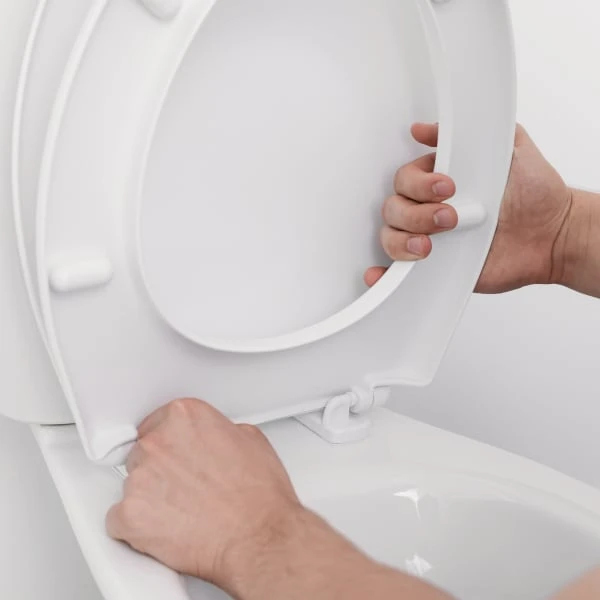 Ruční instalace bílého prkénka na toaletu.
