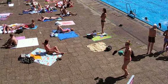 Lidé se opalují na pláži u bazénu v Praze nebo okolí.