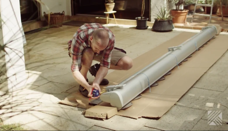 Muž měří markýzu na balkóně během její instalace.