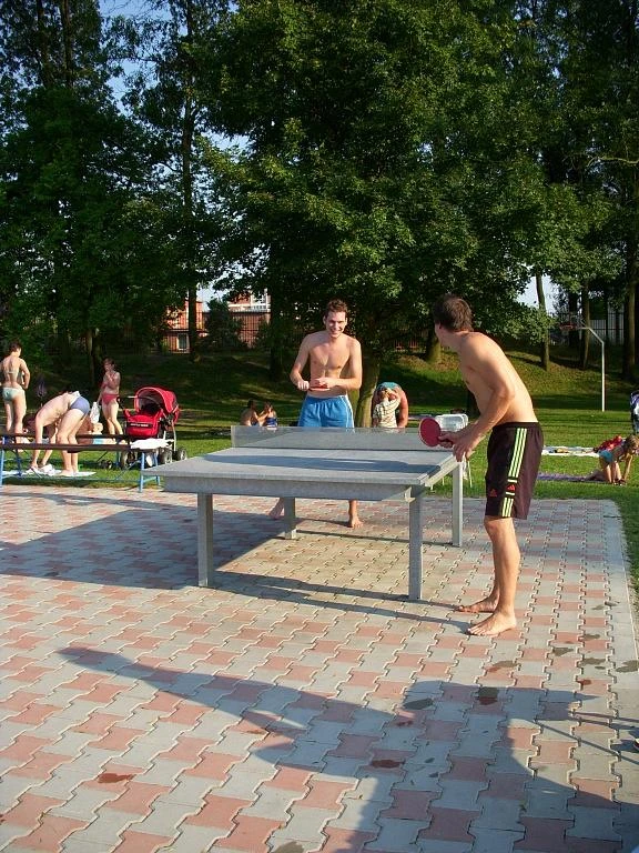 Muži hrají stolní tenis venku na rekreačním místě.