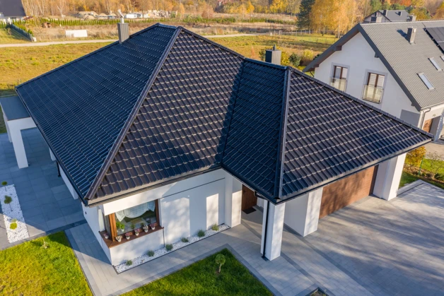 Moderní dům s tmavými střešními taškami na pozadí krajiny.