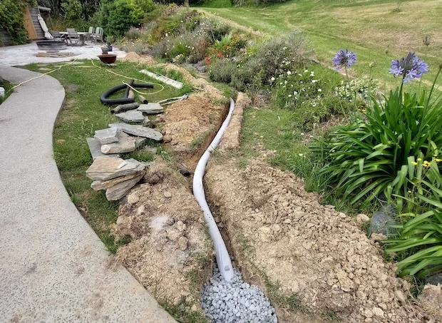 Instalace bílé drenážní trubice v příkopu pro odvodnění zahrady.