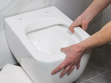 Ruce montují bílou toaletu na podlahu v koupelně.