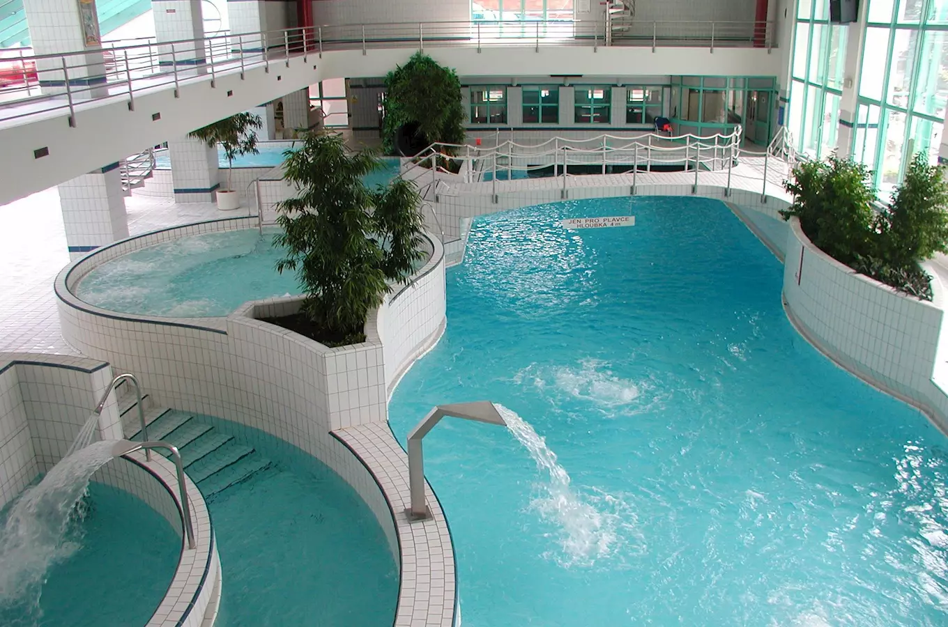Vnitřní plavecký bazén s relaxačními vanami a zelení.