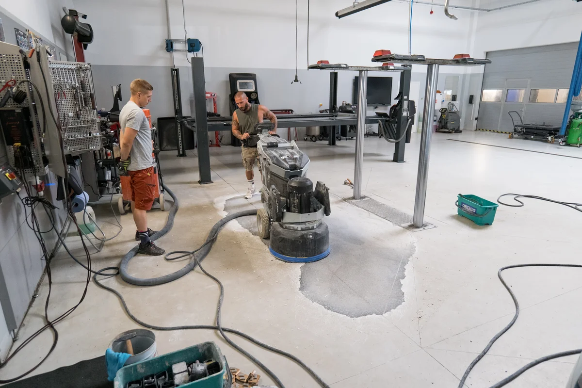 Pracovníci brousí betonovou podlahu v dílně s vysavačem.