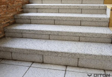 Venkovní betonové schody z dlažebních kostek vedle cihlové zeď.