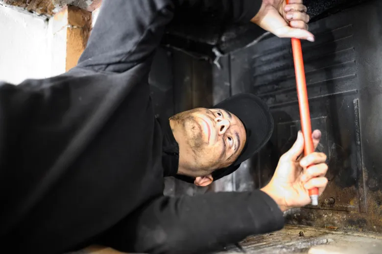 Pracovník provádí revizi komína pomocí nástroje uvnitř spalinové cesty.