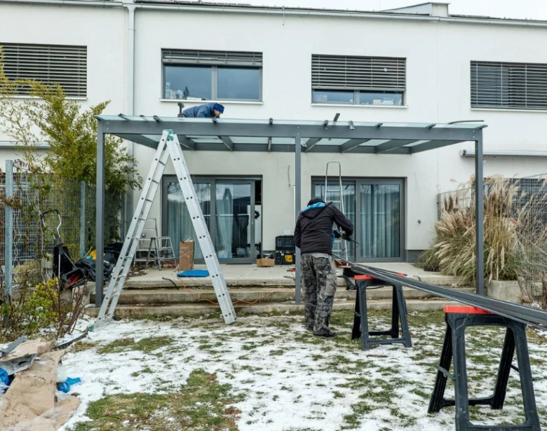 Dva muži staví kovovou pergolu u domu na pozadí sněhu.