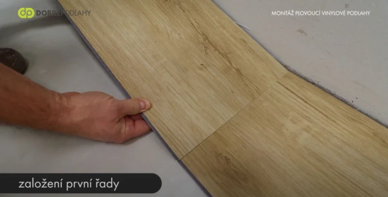 Ruka položí první řadu vinylové podlahy na izolační vrstvu.