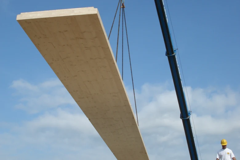 Velký CLT panel je zvedán kranem na staveništi.