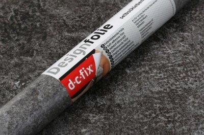 Svinutá samolepicí tapeta DesignFolie od značky dc-fix na šedém pozadí.