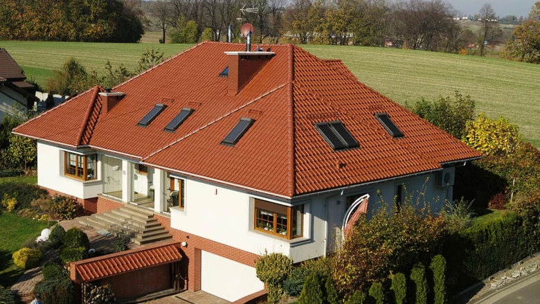 Moderní dům s červenou sedlovou střechou na pozadí zelené krajiny.
