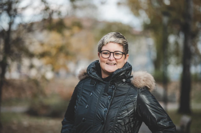 Žena v zimním kabátu stojí venku na pozadí stromů.