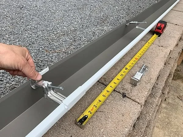 Montáž bílého okapového svodu s držáky na betonu.