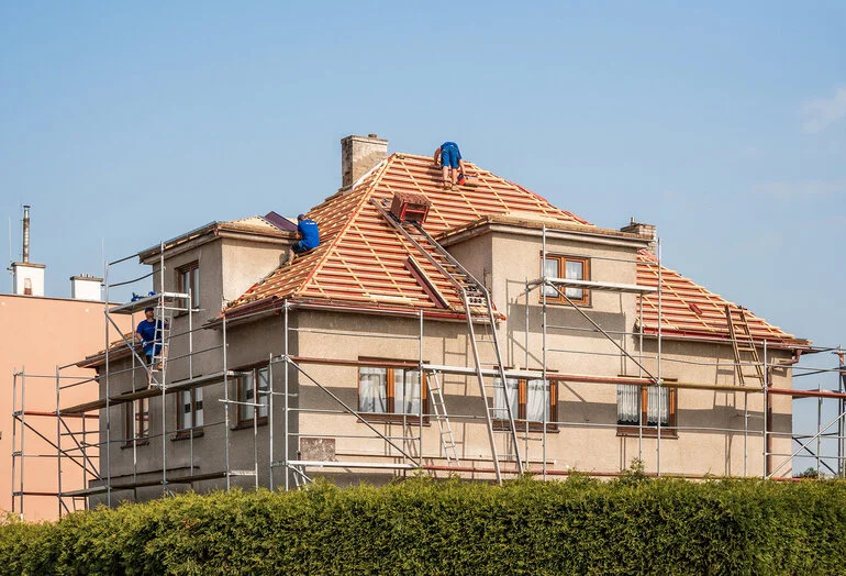 Stavba domu s pracovníky na lešení při rekonstrukci střechy.