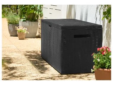 Černý venkovní box na popelnici v zahradě s kvetoucími rostlinami.