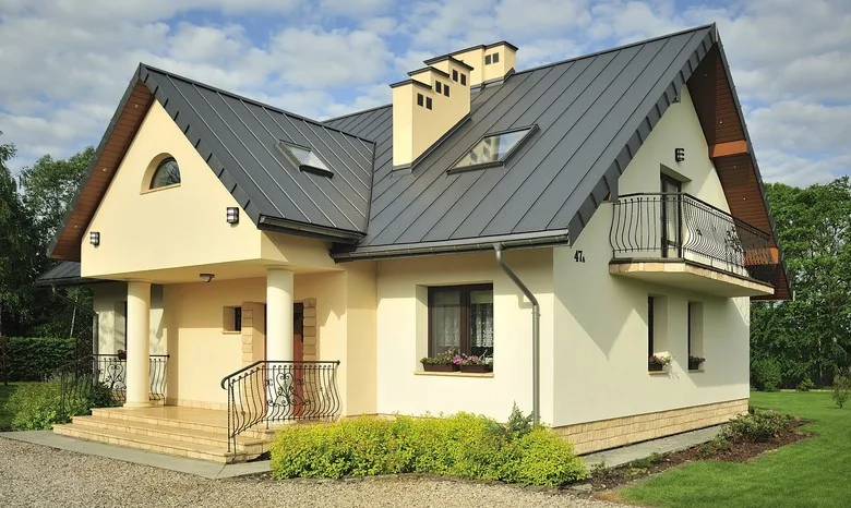 Moderní dům s tmavou plechovou střešní krytinou na pozadí zeleně.