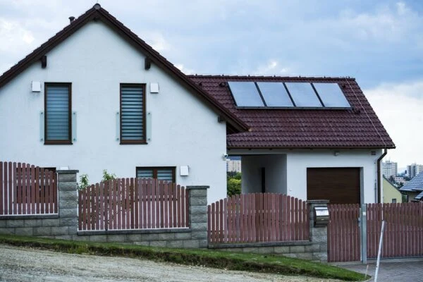 Moderní dům s fotovoltaickými panely a dřevěným plotem.