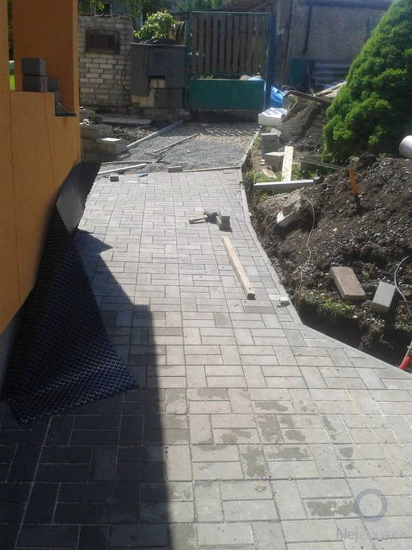 Pokládka zámkové dlažby na zahradě s nástroji a materiály.